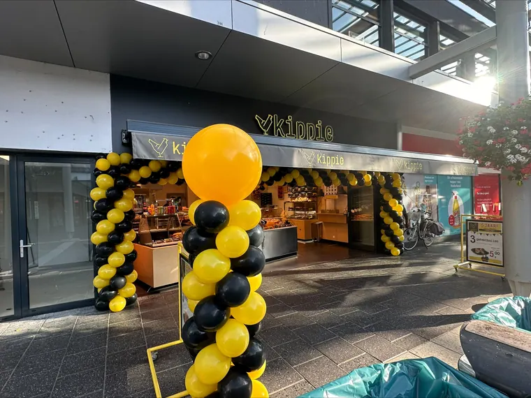 Geel-zwarte pilaar en boog bij een winkelopening